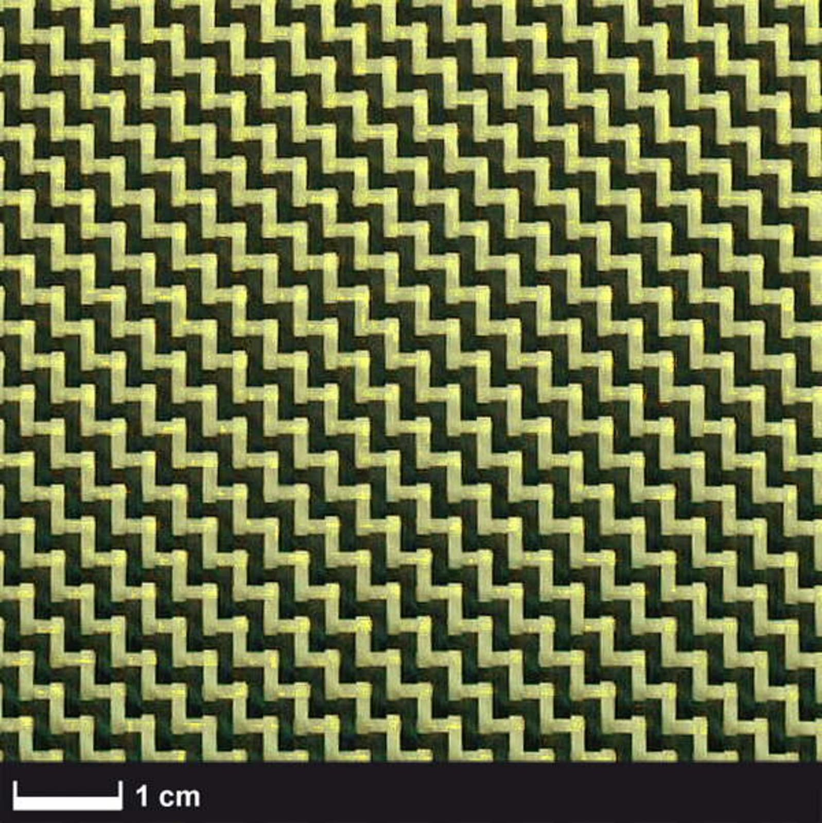 The image shows a close-up of a woven fabric with a zigzag pattern. The fabric has alternating light and dark strands, creating a textured appearance. A scale bar indicating 1 cm is visible at the bottom.