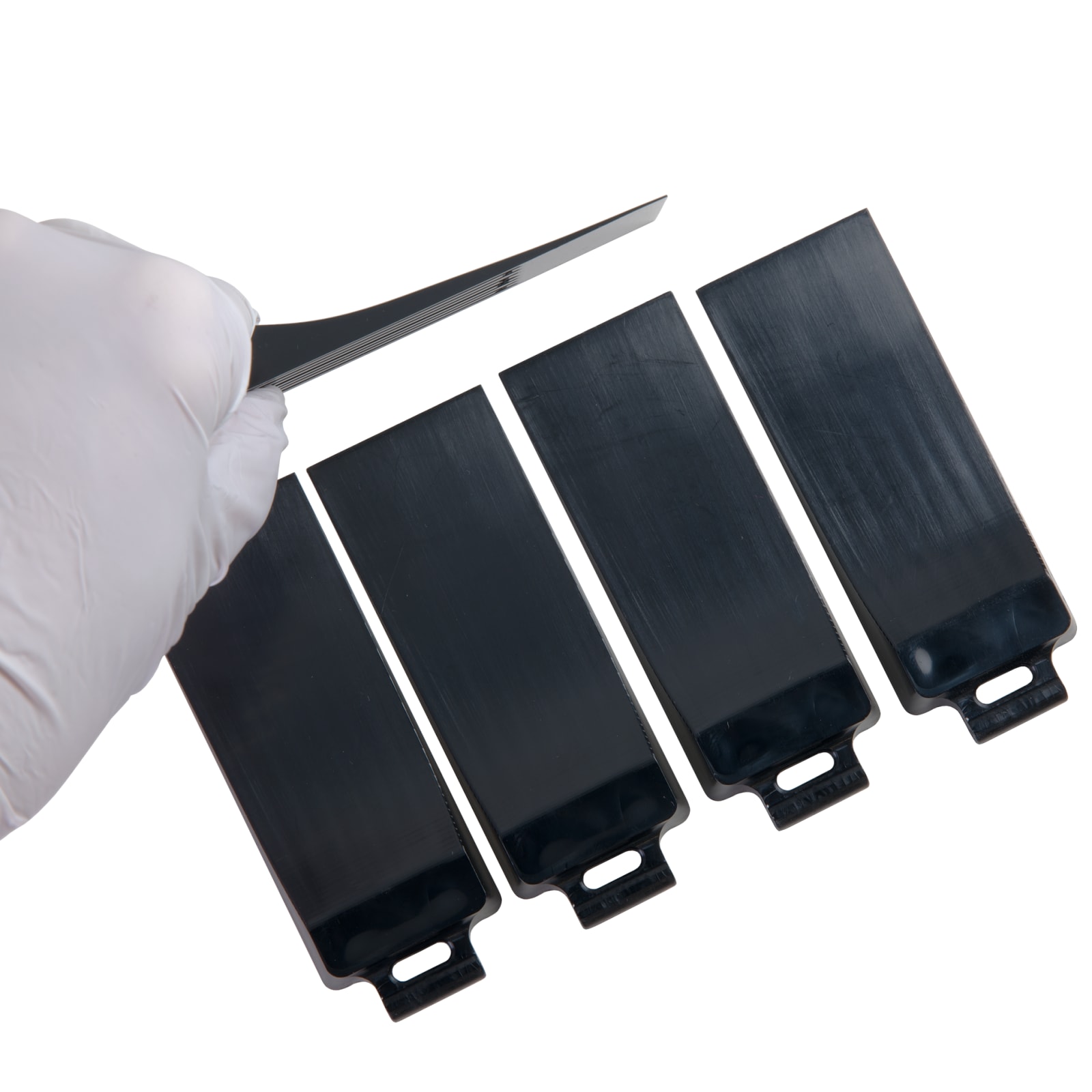 A gloved hand is holding a black demoulding wedge above four black demoulding wedges arranged in a row.