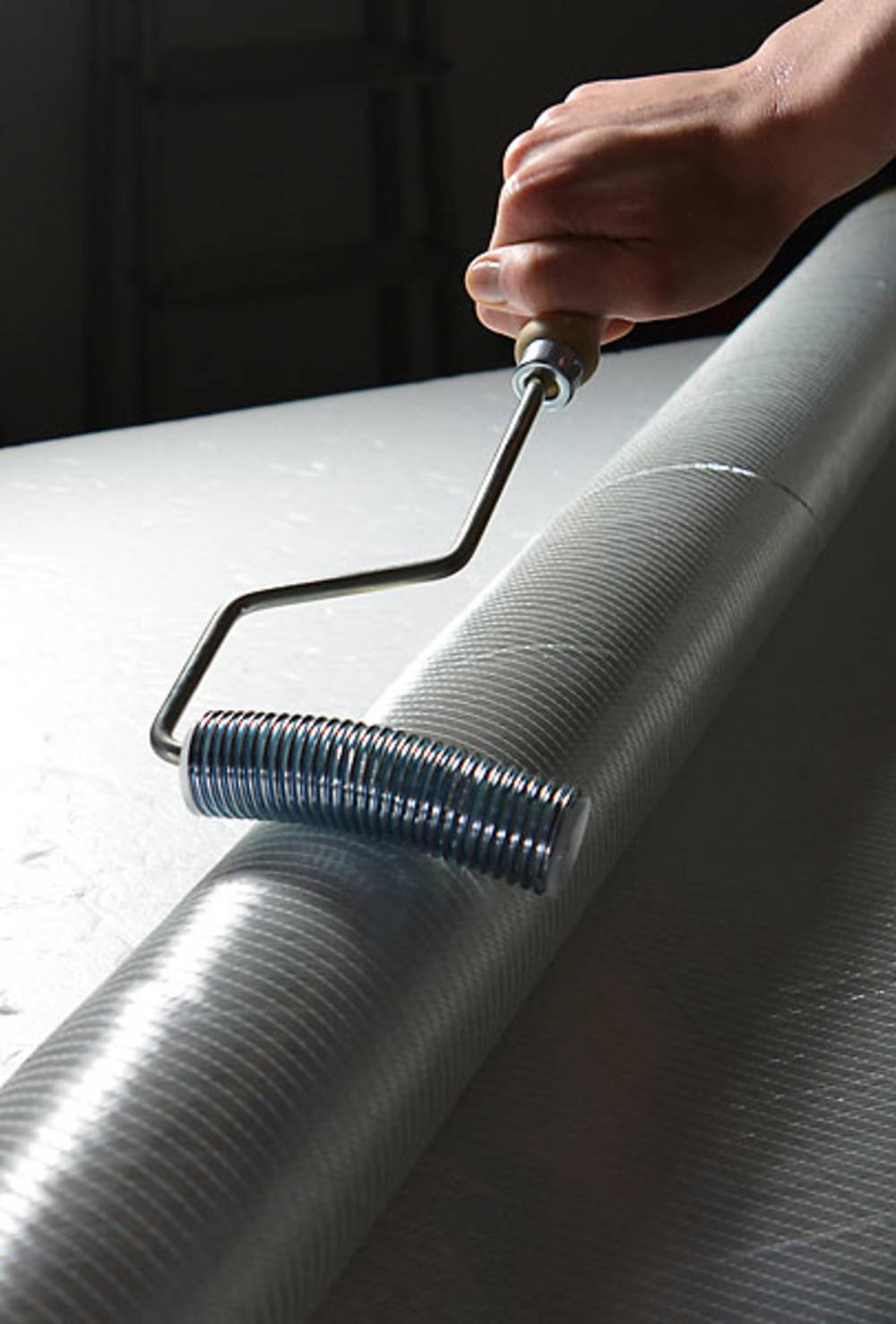 Eine Hand hält einen Metallroller über einer großen, zylindrischen Oberfläche.