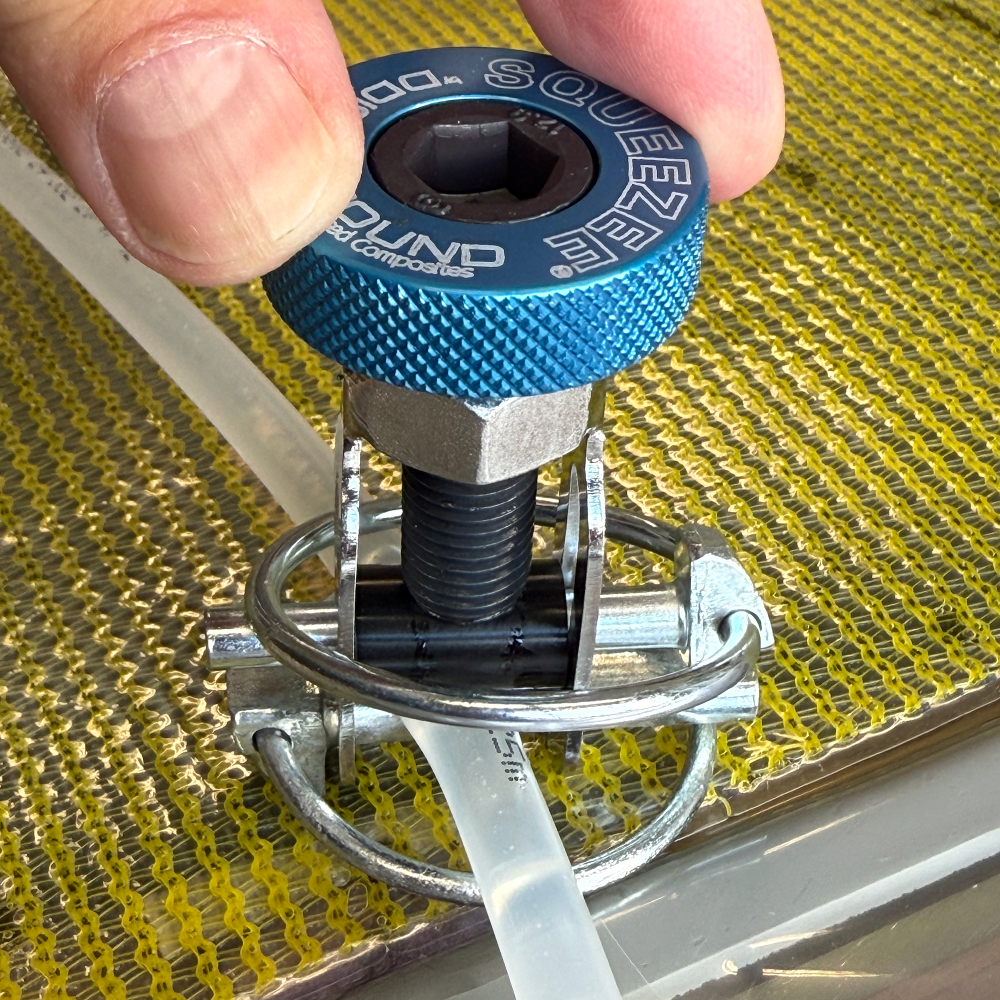 Ein blauer Squeezer-Werkzeugkopf wird von einer Hand gehalten, um eine durchsichtige Röhre auf einer gelben Oberfläche zu komprimieren.