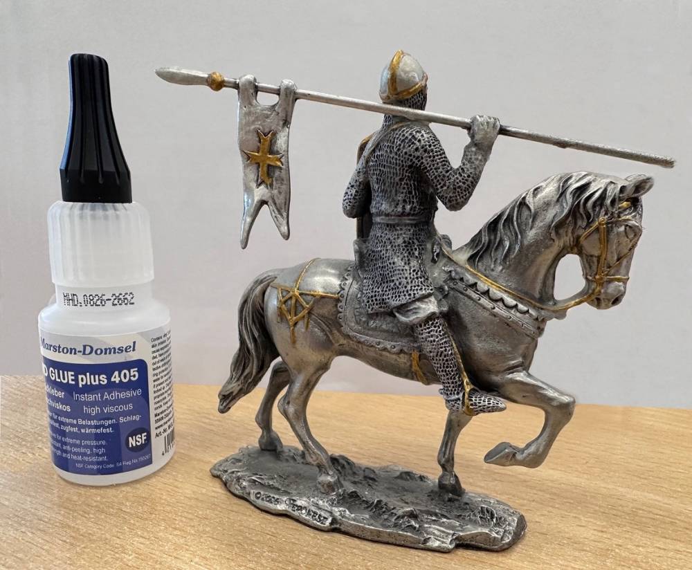 Eine Ritterfigur auf einem Pferd mit einer Lanze, daneben eine Flasche Kleber. 