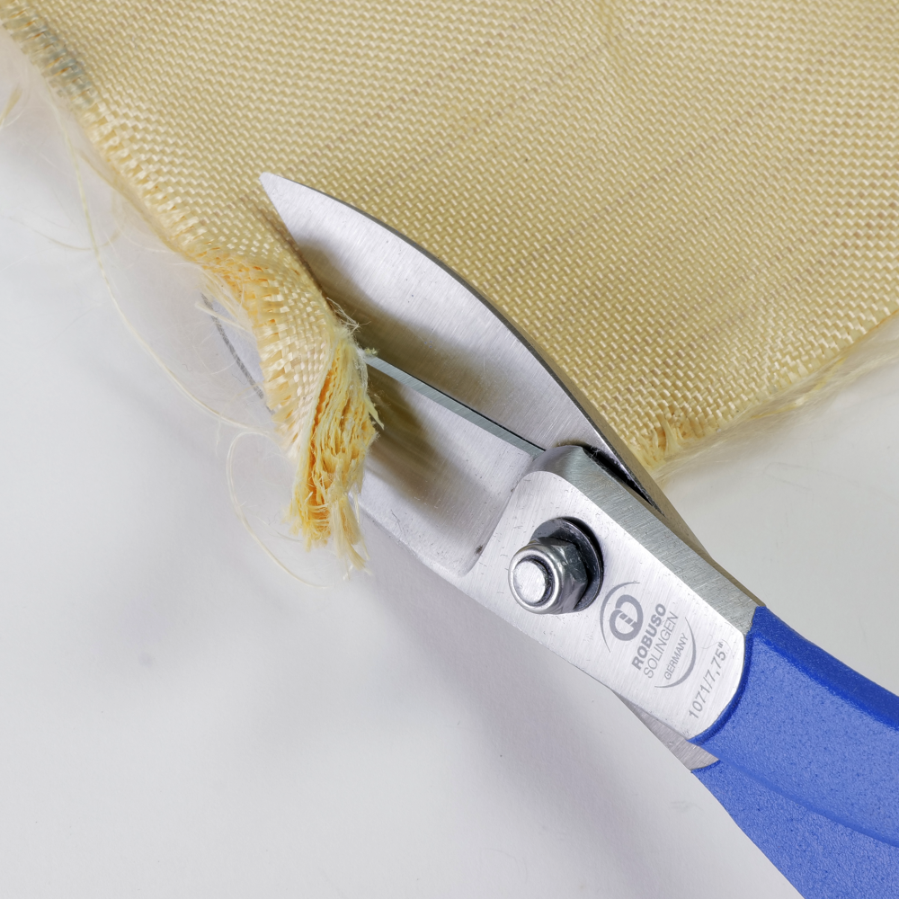 Scissors cutting a piece of woven fabric. The scissors have blue handles and a metallic blade. The fabric is beige and frayed at the edge.