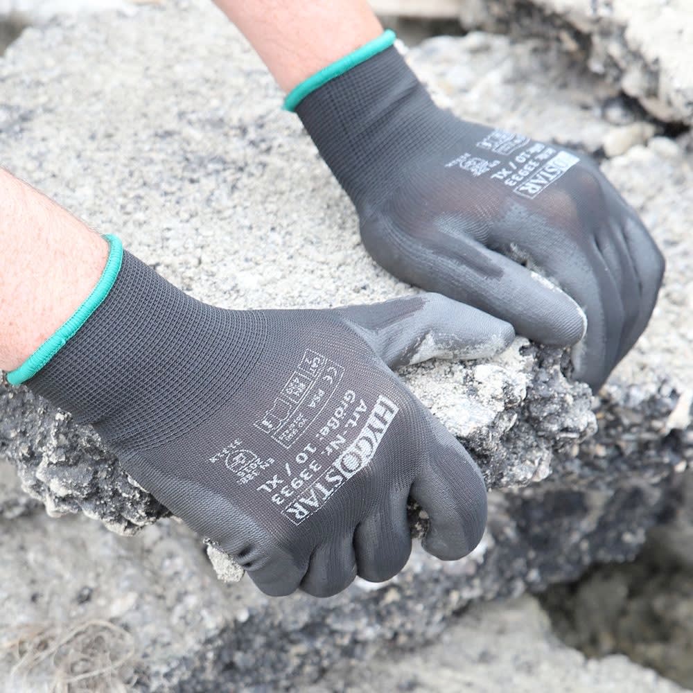 Zwei Hände in schwarzen Arbeitshandschuhen halten ein Stück Beton oder Asphalt.