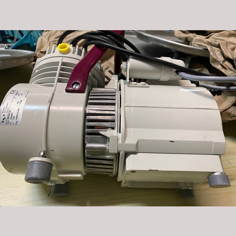 A close-up view of a vaccum pump, with a beige body, red handle, and visible wiring and components.