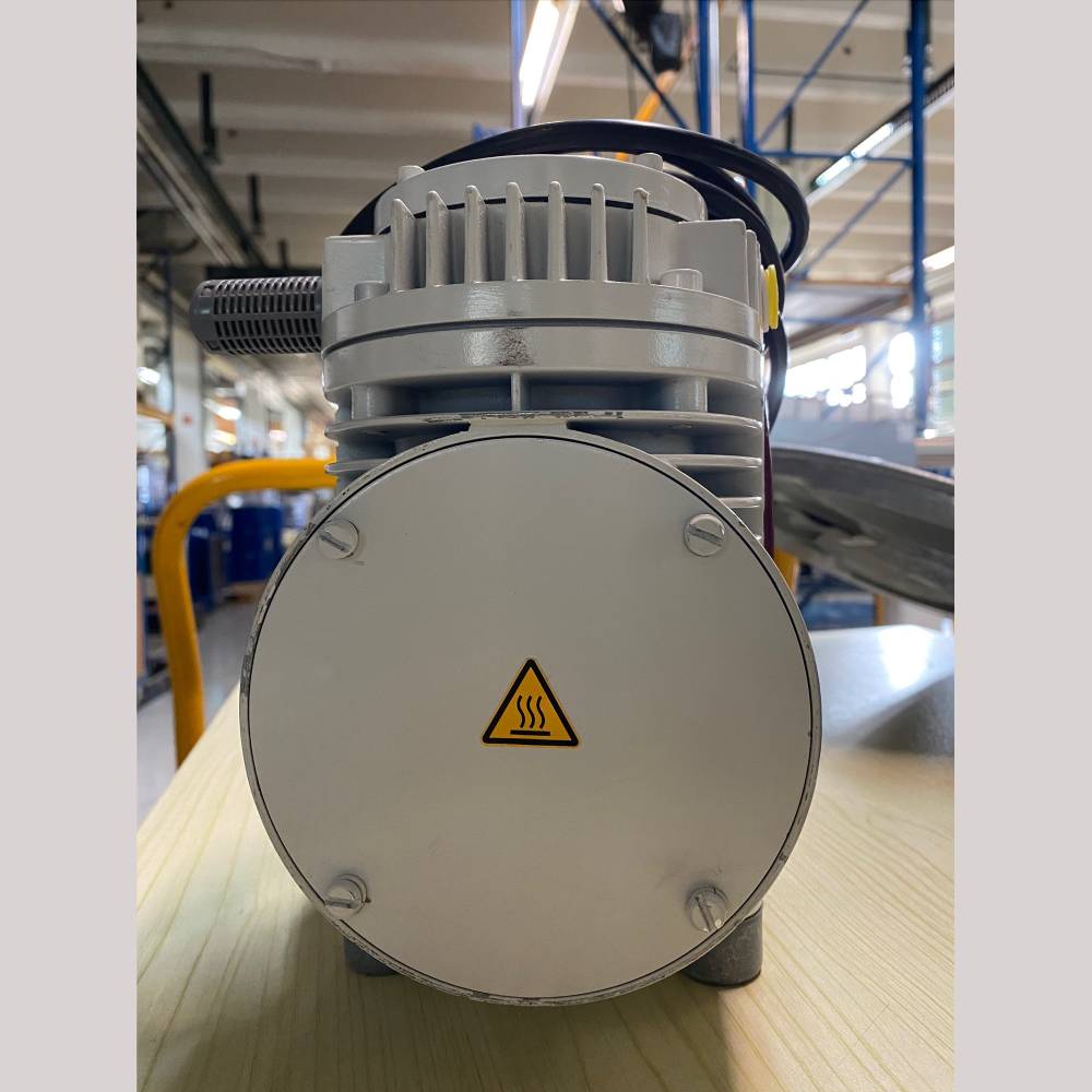 A close-up of a vacuum pump with a heat warning symbol in a factory setting.