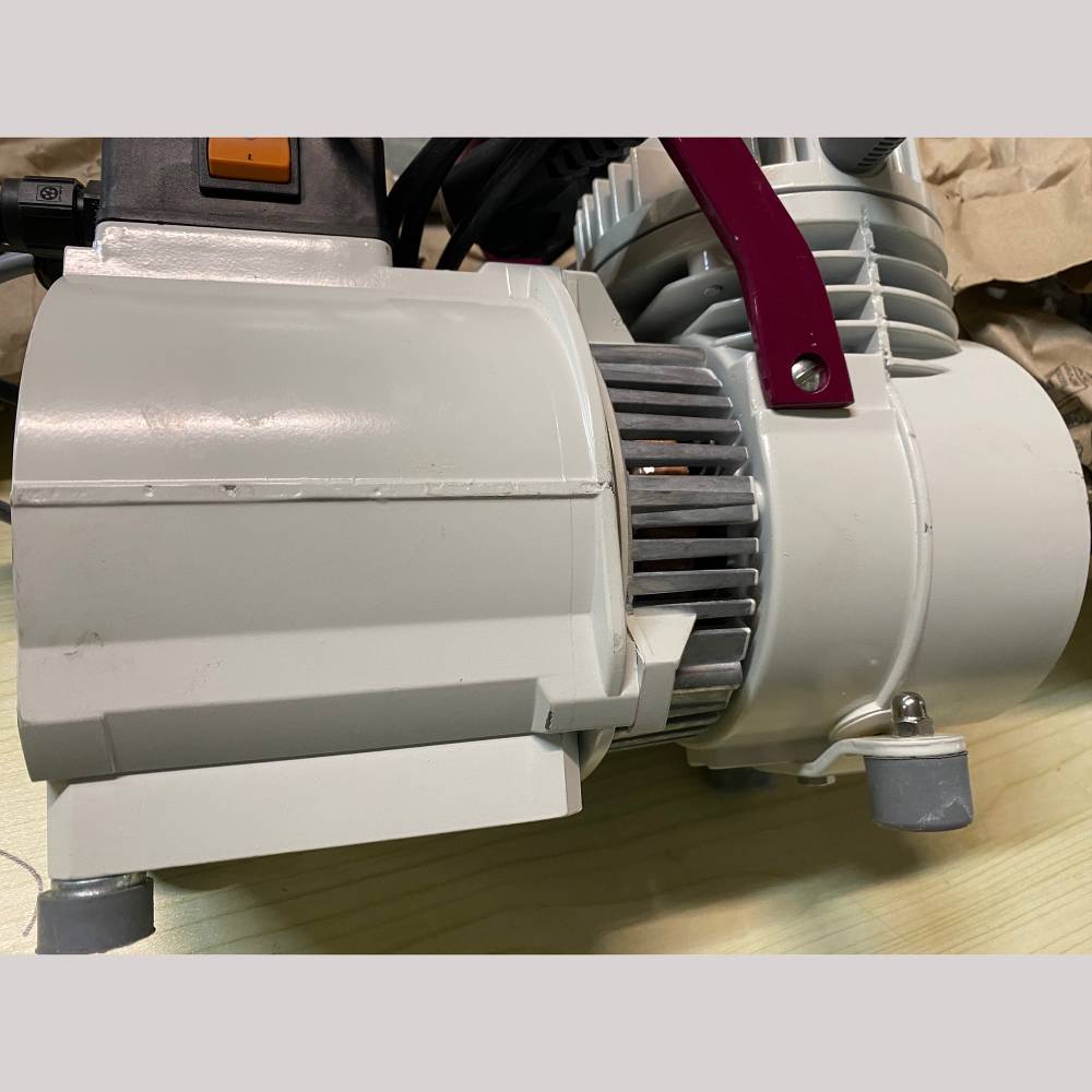 The picture shows a gray vacuum pump on a table. It has cooling fins and a red handle.