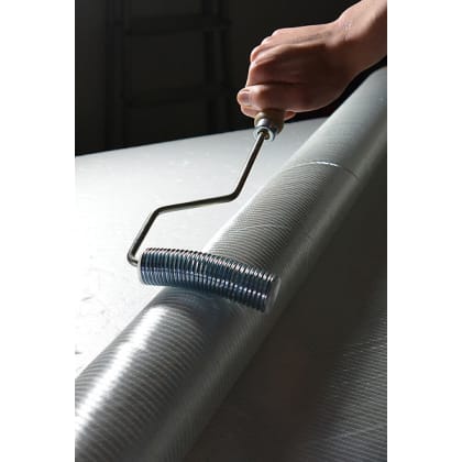 Eine Hand hält einen Metallroller über einer großen, zylindrischen Oberfläche.