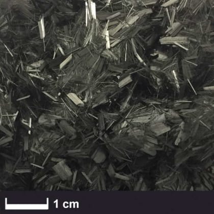 Nahaufnahme von schwarzen Fasern oder Spänen mit unregelmäßiger Form, Maßstab zeigt 1 cm.