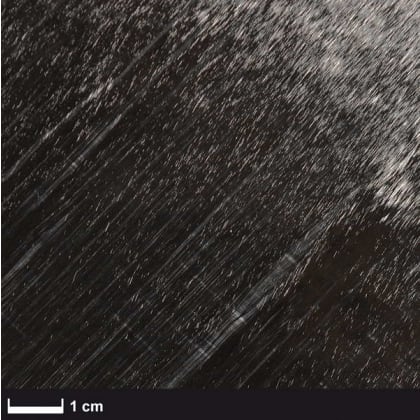 Nahaufnahme einer Oberfläche mit diagonalen Kratzern und einer Maßstabsleiste von 1 cm.