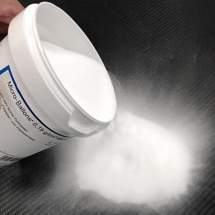 Ein Behälter mit der Aufschrift “Micro Balloons“ wird geneigt, um ein weißes Pulver auf eine Oberfläche zu schütten.